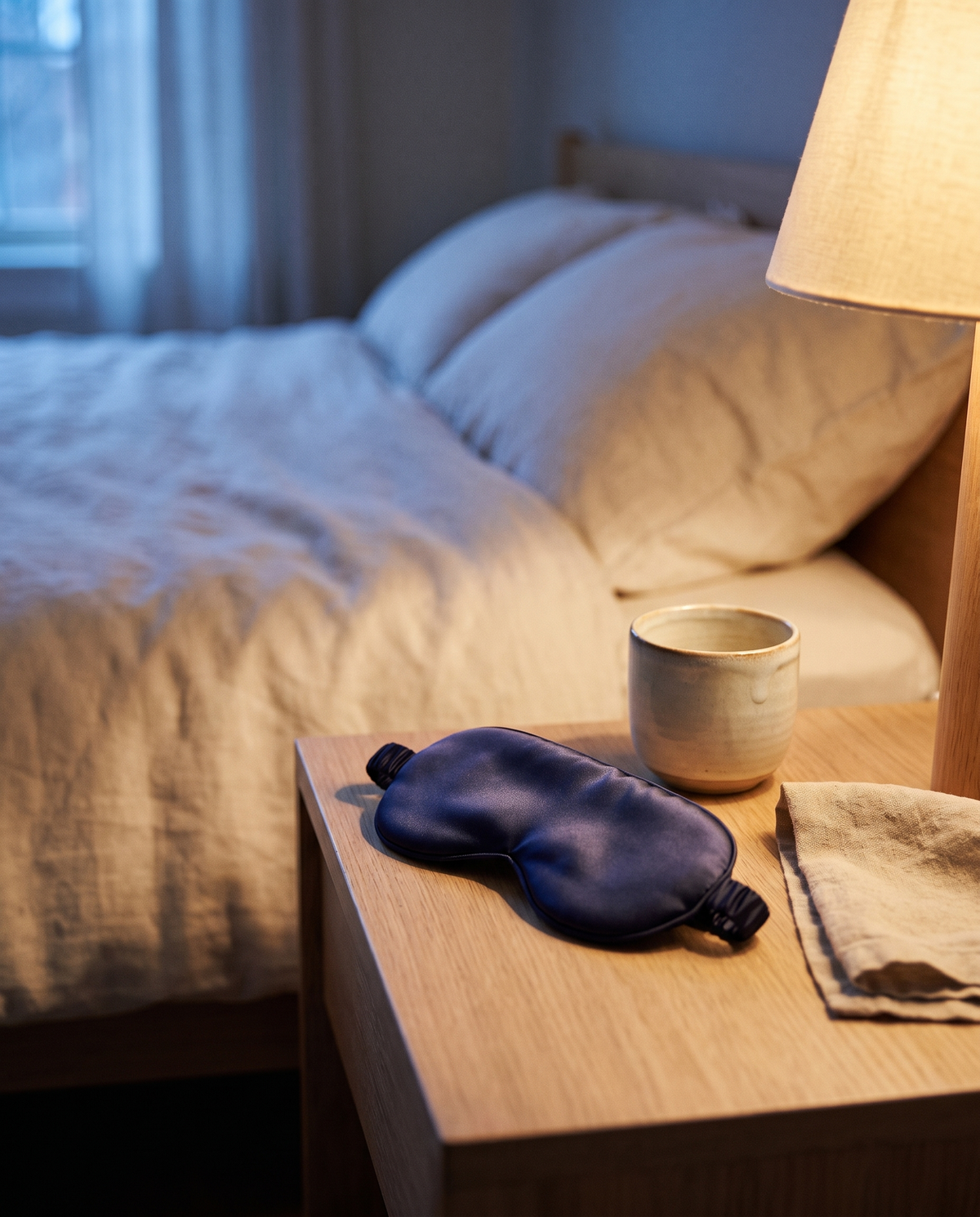 Le masque en soie posé sur une table de nuit en bois clair
