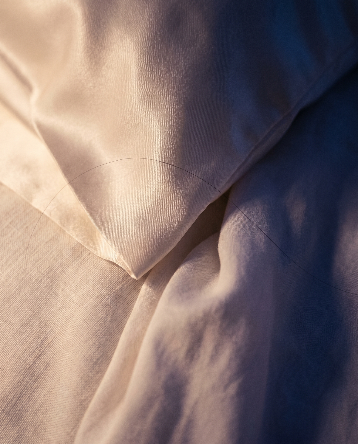 Gros plan sur le satin de la taie, à côté du grain mat du lin
