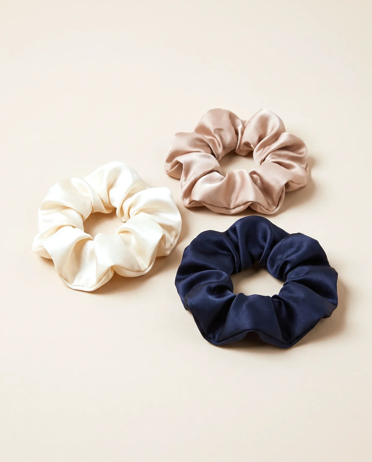 Trois chouchous en satin, crème, beige et bleu nuit, sur fond sable