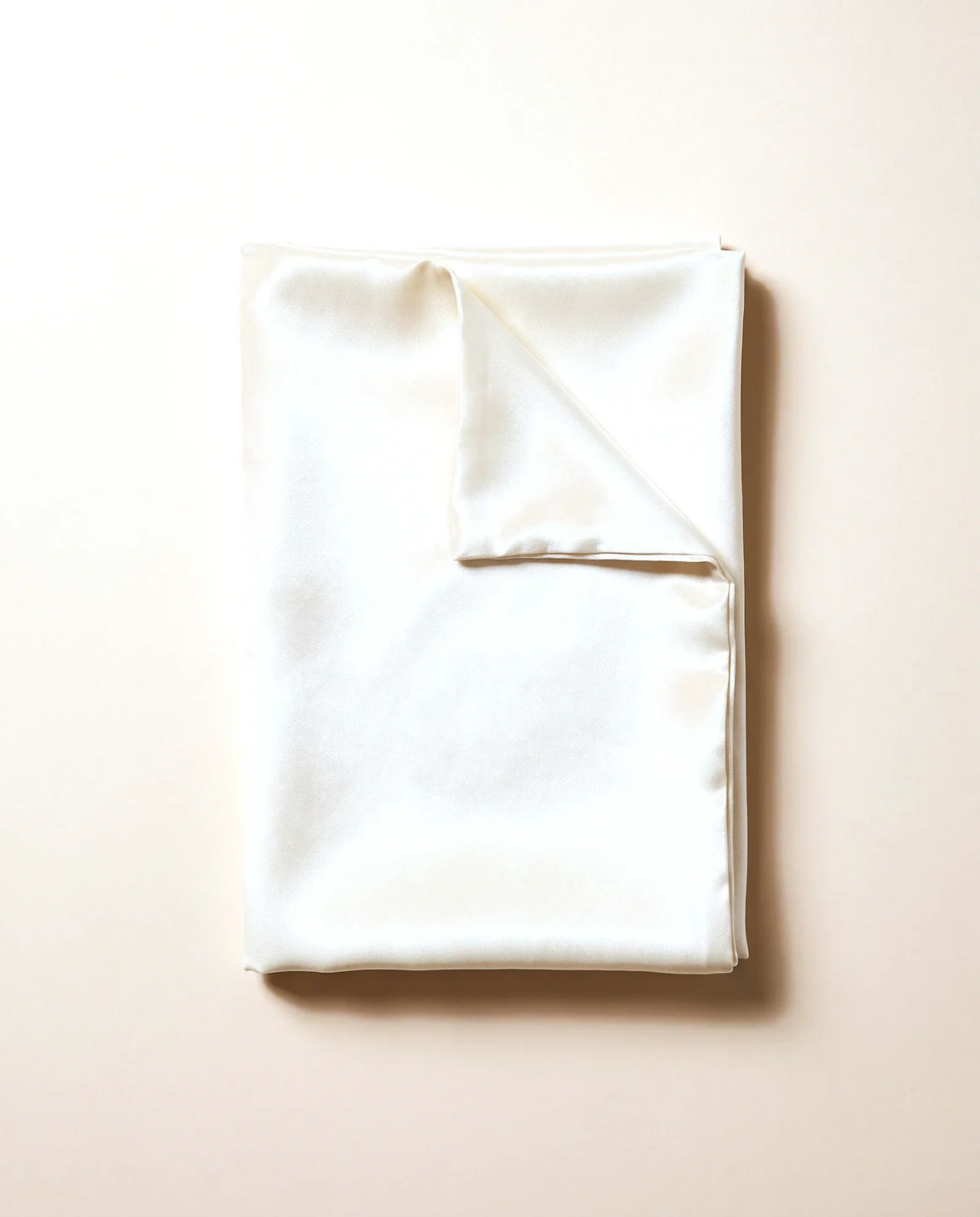 Taie d'oreiller en satin crème, pliée, sur fond sable